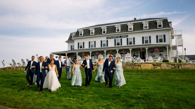 A group of people, some in formal attire, are walking on a grassy field in front of a large, white building labeled 