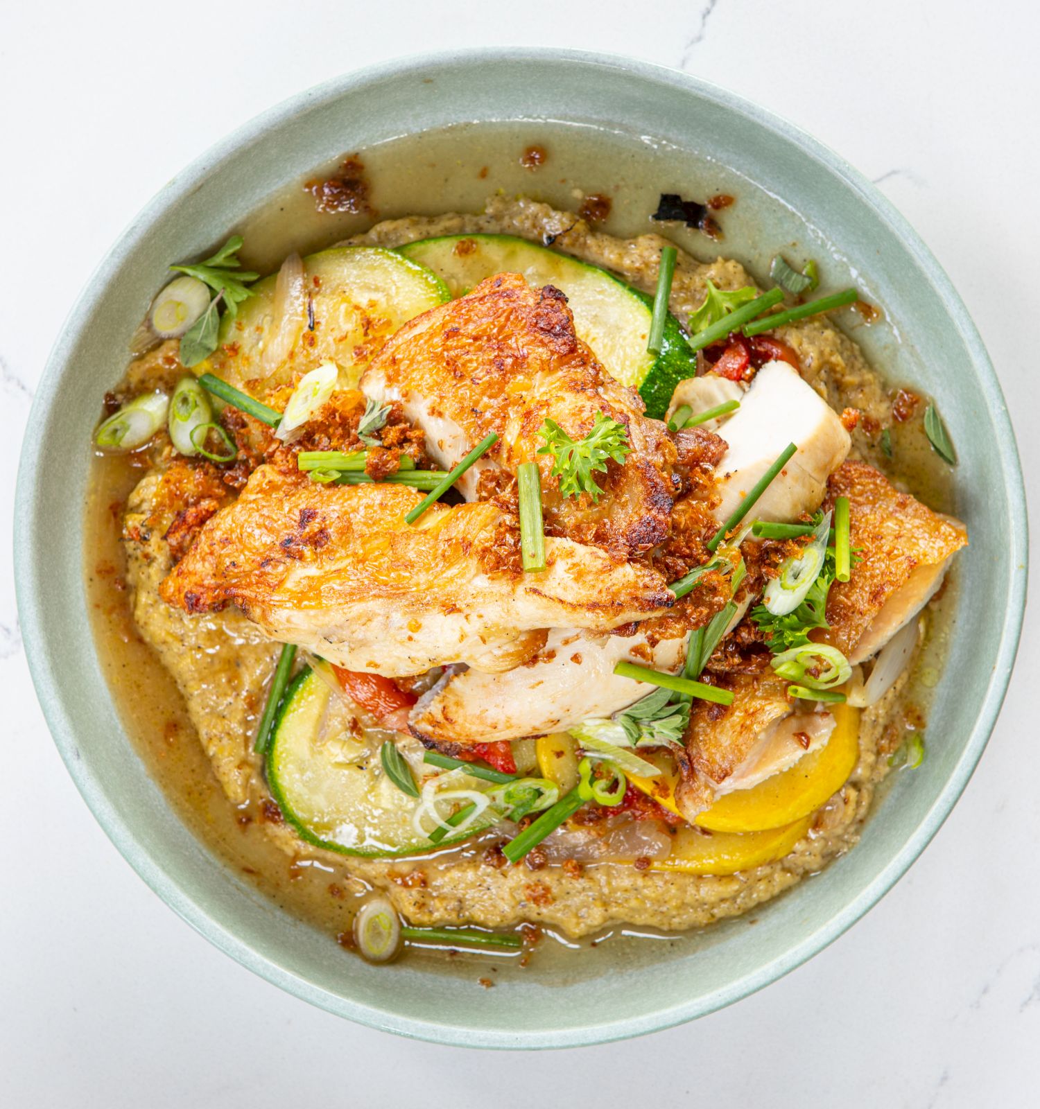 The image shows a bowl with fish fillets, vegetables, and garnished with green onions over a creamy base.