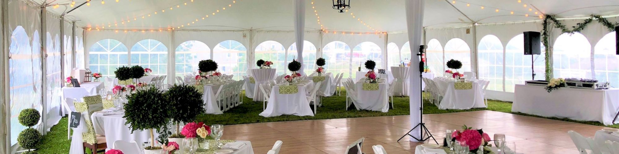 The image shows a beautifully decorated event tent with tables set up for a formal gathering. There are string lights and elegant floral arrangements.