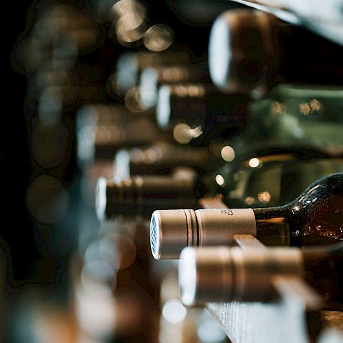 The image shows several bottles of wine stored on their sides in a wine rack, with a blurred background.