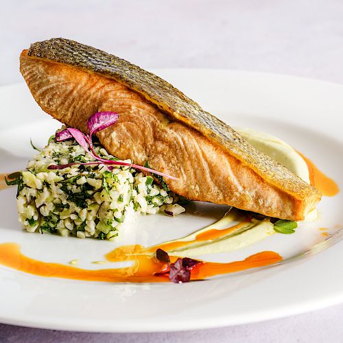 The image features a beautifully plated dish with a cooked fish fillet, herb-infused rice, and garnishes, drizzled with sauce on a white plate.