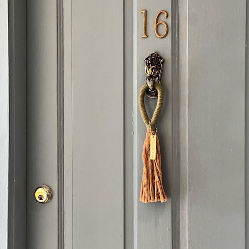 A grey door with the number 16 and a knocker adorned with an orange tassel.