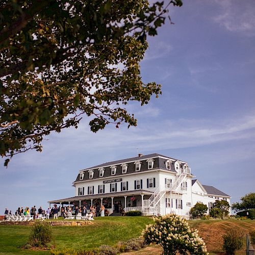 A large white building, possibly a hotel or mansion, surrounded by green lawns and trees under a partly cloudy sky.