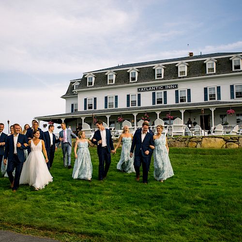 A bridal party in formal attire walks across a lawn in front of a large, white building that says 