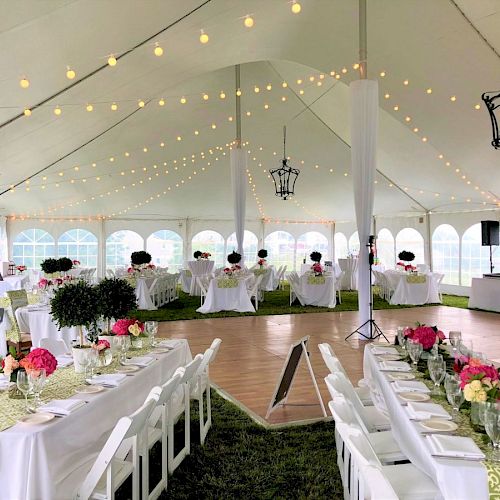 A decorated white tent for an event with tables, chairs, floral centerpieces, string lights, and a wooden dance floor set up inside.