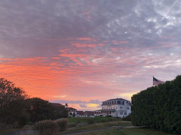 The image shows a scenic landscape with a large house, a vivid sunset sky, trees, and a flagpole with a waving flag, creating a picturesque view.