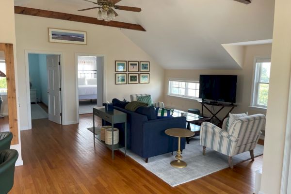 A cozy living room with wooden flooring, a blue sofa, striped chairs, a TV on a stand, framed wall art, and a ceiling fan, ending the sentence.