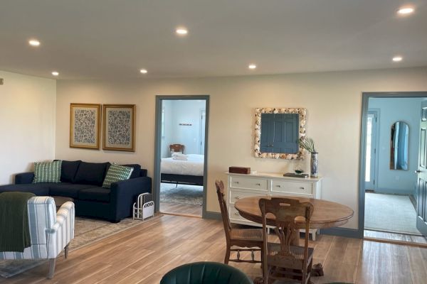 A cozy, furnished living room with a blue sofa, armchairs, a dining table, and wall art, leading to other rooms through doorways.