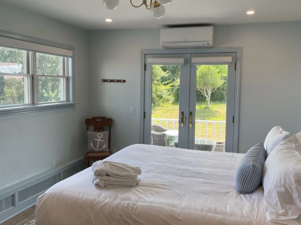 A well-lit bedroom with a large bed, folded towels, windows, glass doors leading outside, and a wall-mounted air conditioner.