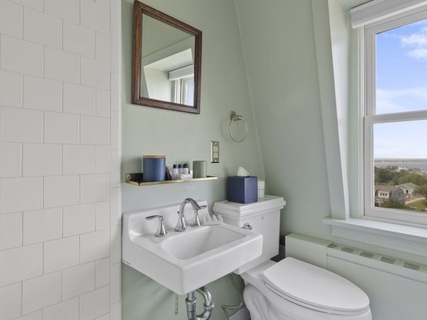 A bathroom with a sink, toilet, mirror, and window overlooking a landscape. There is a shelf above the sink with toiletries.
