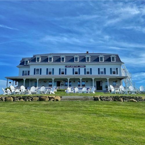 The image shows a large, multi-story white house with a wide porch, surrounded by green grass under a blue sky.