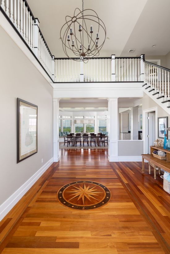 A modern hallway with wooden flooring, decorative ceiling light, and staircase, leading to a dining area with a table and chairs.