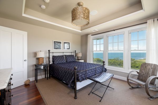 A cozy bedroom with a double-bed, large windows offering a scenic ocean view, wooden floor, and neutral decor creates a relaxing ambiance.