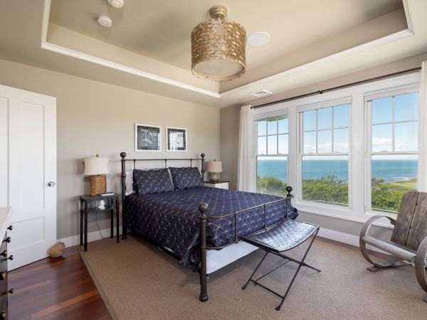 A cozy bedroom with a double-bed, large windows offering a scenic ocean view, wooden floor, and neutral decor creates a relaxing ambiance.