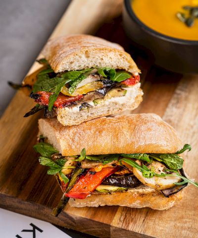 A grilled veggie sandwich with crusty bread, leafy greens, roasted peppers, mushrooms, and melted cheese, ready to eat.