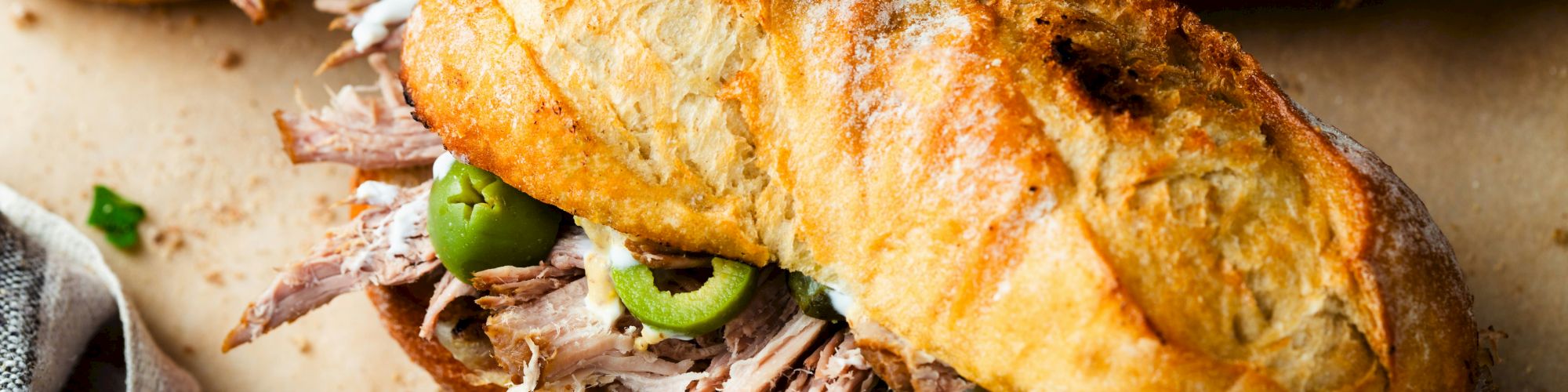 A toasted bread roll stuffed with pulled pork, melted cheese, and sliced green peppers on a rustic table.