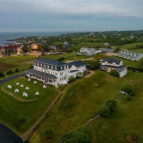 The image shows a coastal resort with large houses, lush green landscapes, and a view of the ocean. It appears to be taken at dusk.