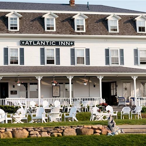 The image depicts the Atlantic Inn, a white colonial-style building, with a front porch and lawn seating arranged for guests.