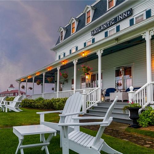 A charming inn with a porch and white wooden chairs on a manicured lawn, under a pastel sky.