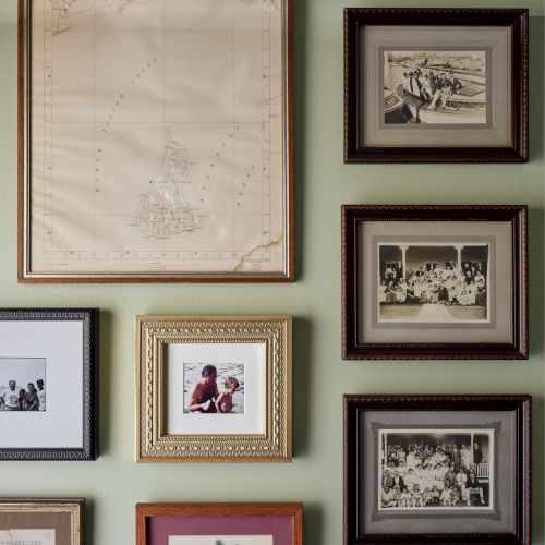 A variety of framed pictures and a map are arranged on a light green wall, including black-and-white photos and a colored artwork.