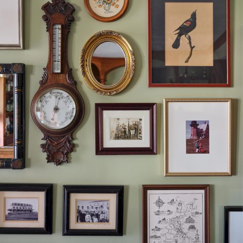 A wall with various framed artworks, a vintage barometer, and a mix of illustrations and photos in different styles and sizes.