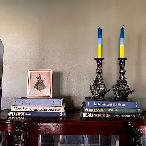 A bookshelf with stacked books, a framed picture, and two ornate candlesticks with blue and yellow candles.