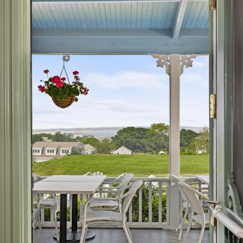 A small porch view overlooking a green lawn and lake, with a hanging plant basket and white railing, inviting outdoor relaxation.